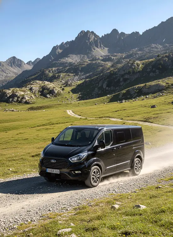 Furgoneta 4x4 negra en camino de alta montaña con paisaje verde y picos rocosos del Pirineo.
