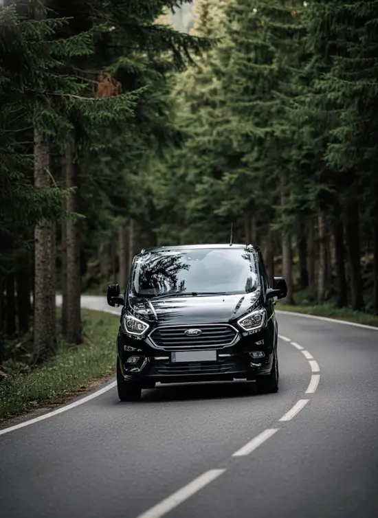 Furgoneta negra Ford Tourneo Custom circulando por carretera de bosque en el Valle de Arán.