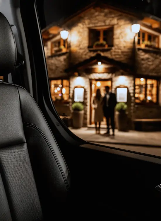 Interior de vehículo de lujo de noche frente a restaurante iluminado. Servicio de chófer para cenas.