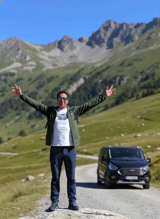 Luis Luengo, anfitrión y guía de AranDrive, saludando con los brazos abiertos en las montañas del Val d'Aran junto a su taxi.